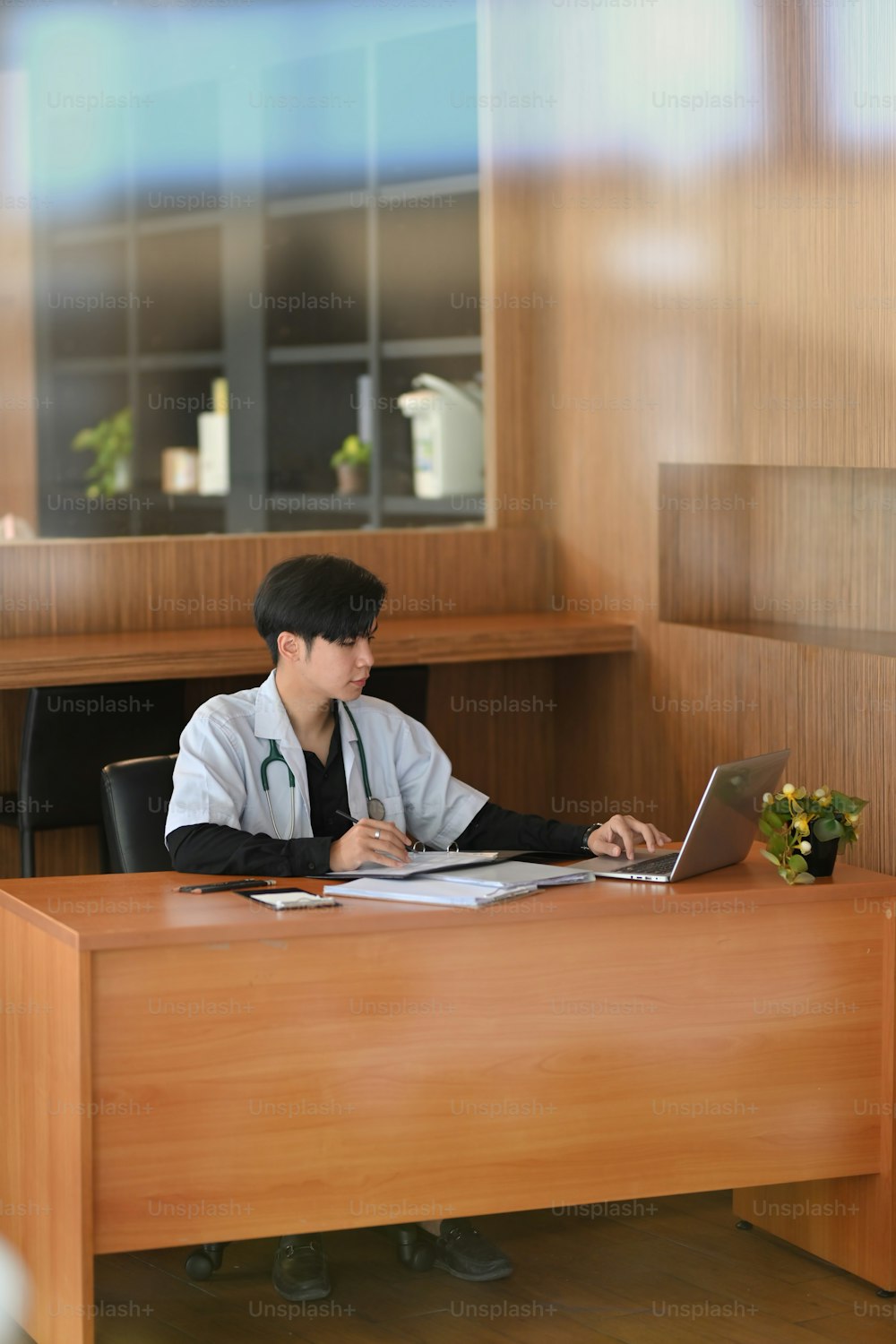 Male doctor working at his office desk, writing a medical email on laptop computer, checking an online prescription form