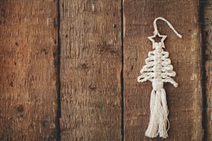 Elegante ornamento de macramê de árvore de Natal borda em madeira rústica flat lay. Ornamento de árvore boho feito à mão para o feriado de Natal. Feliz Natal! Decoração escandinava, brinquedo ecológico. Espaço para texto