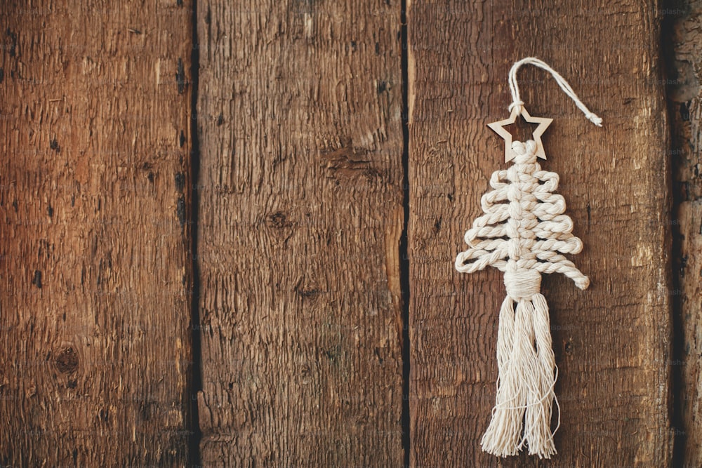 Elegante bordo ornamentale macramè per albero di Natale su legno rustico flat lay. Ornamento dell'albero boho fatto a mano per le vacanze di Natale. Buon Natale! Arredamento scandinavo, giocattolo ecologico. Spazio per il testo