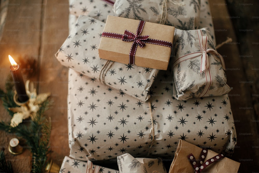 Frohe Weihnachten! Stilvolle Weihnachtsgeschenke eingewickelt in Bastelpapier, Vintage-Kerzen, Tannenzweige und Glocken auf rustikalem Holz. Stilvolle skandinavische Weihnachtsgeschenke, stimmungsvolle Winterzeit auf dem Land