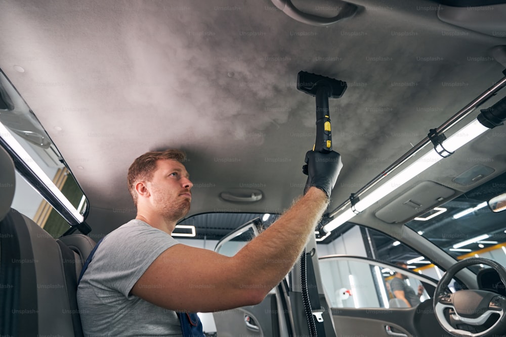 Service worker using vapor cleaner for automobile cabin. Steam sterilizing. Dry cleaning car salon