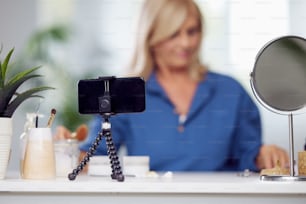 A senior vlogger sitting at home and talking about new beauty products. Focus on foreground