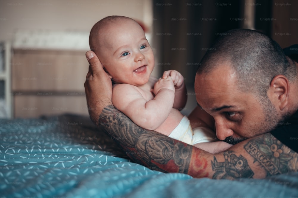Tattooed bearded father playing with his son in diapers while at home