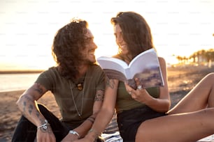 Beautiful happy couple on a date,  reading a book on the tropical beach. Summer vacation vibes. Sunset time.