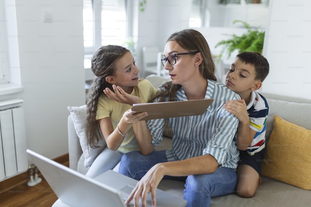 Femme travaillant à domicile pendant la quarantaine avec son petit fils et sa petite fille sur le canapé et criant, exigeant de l’attention