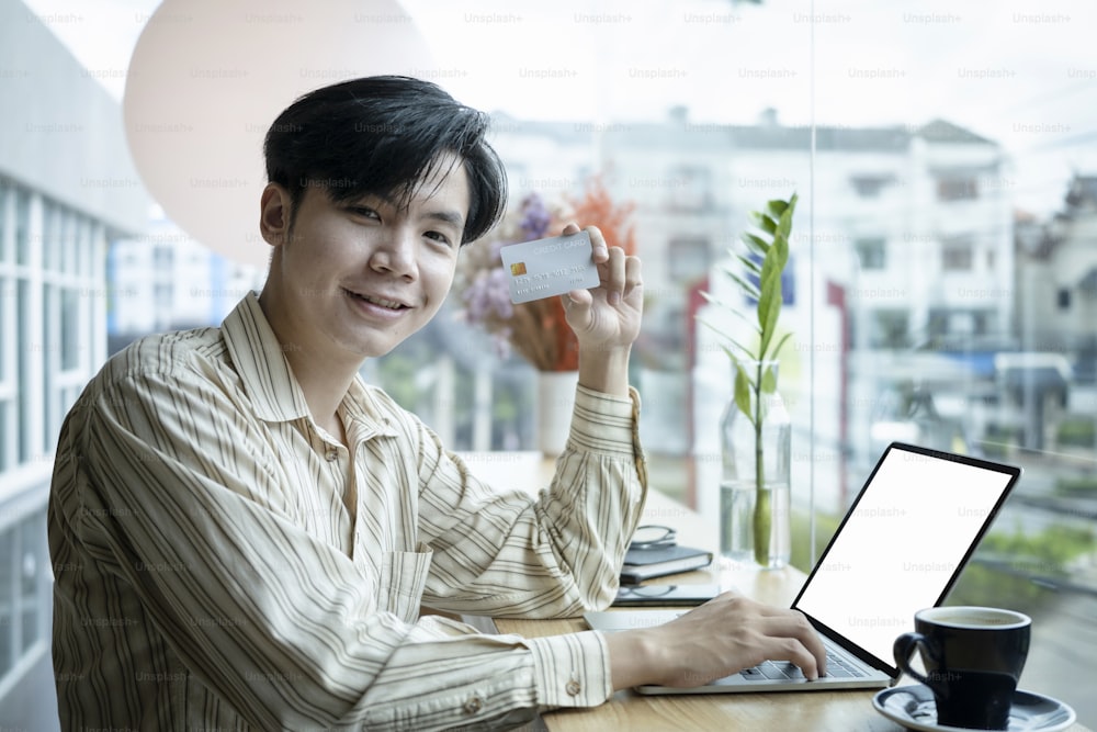 Cheerful young Asian man holding credit card and smiling to camera.