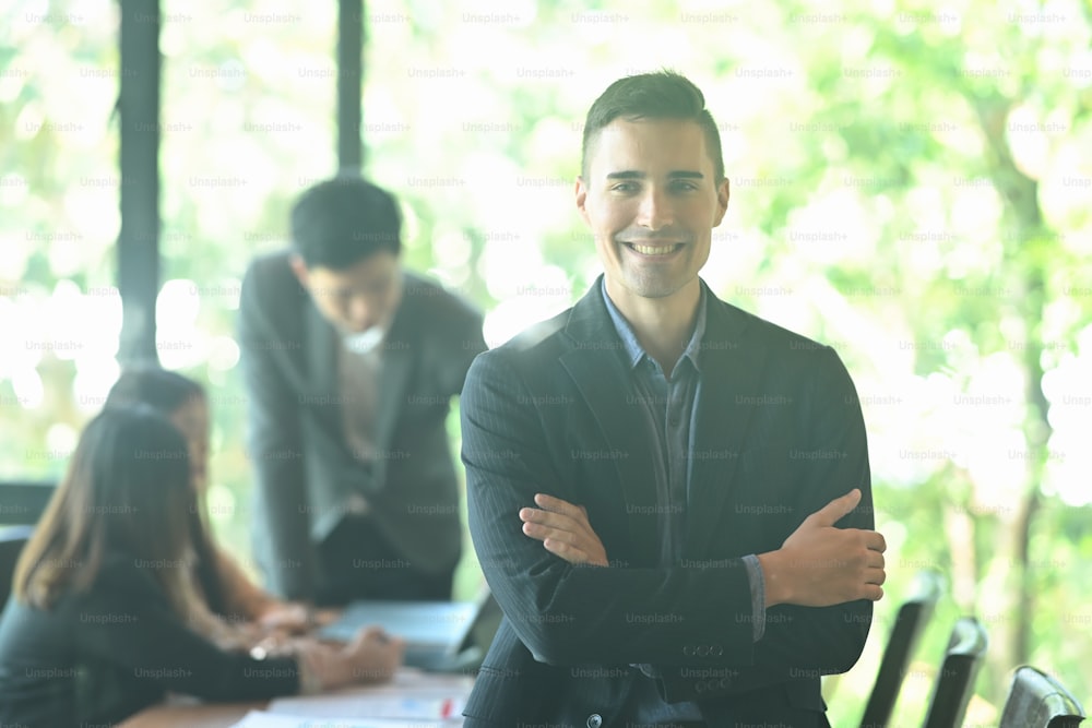 Successful businessman standing with crossed arms in meeting room.