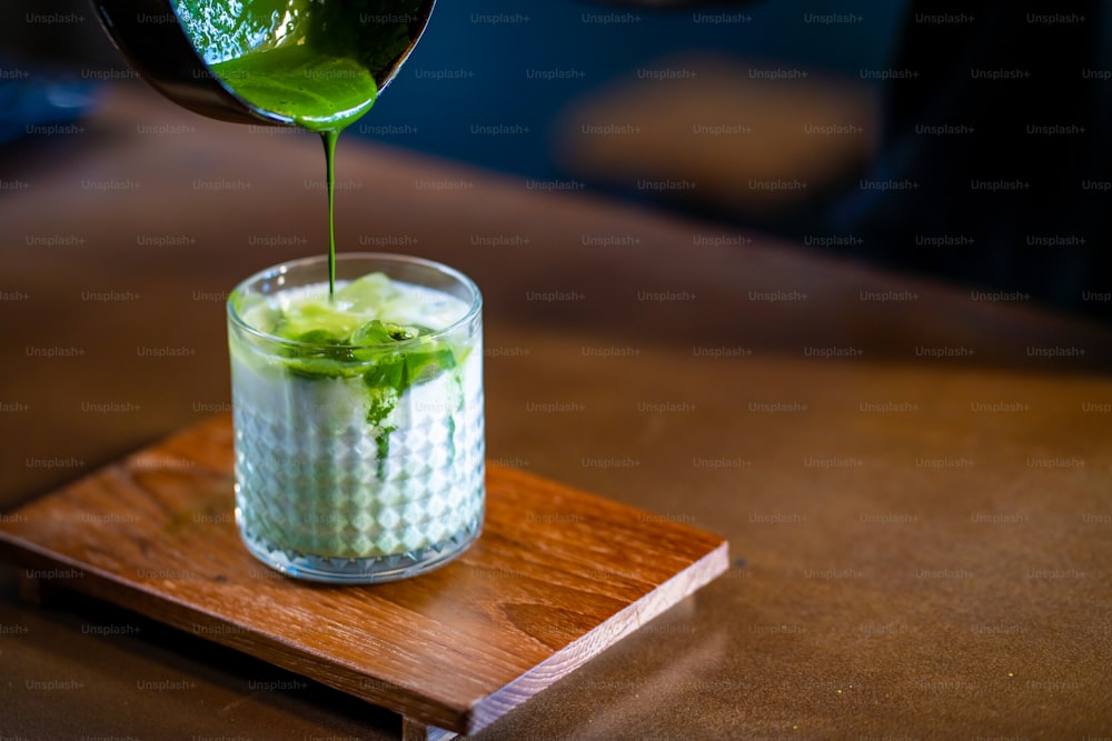 Asian woman barista making matcha green tea with fresh milk in the glass. Female coffee shop waitress serving iced matcha latte to customer on counter at cafe. Small business coffee shop owner concept