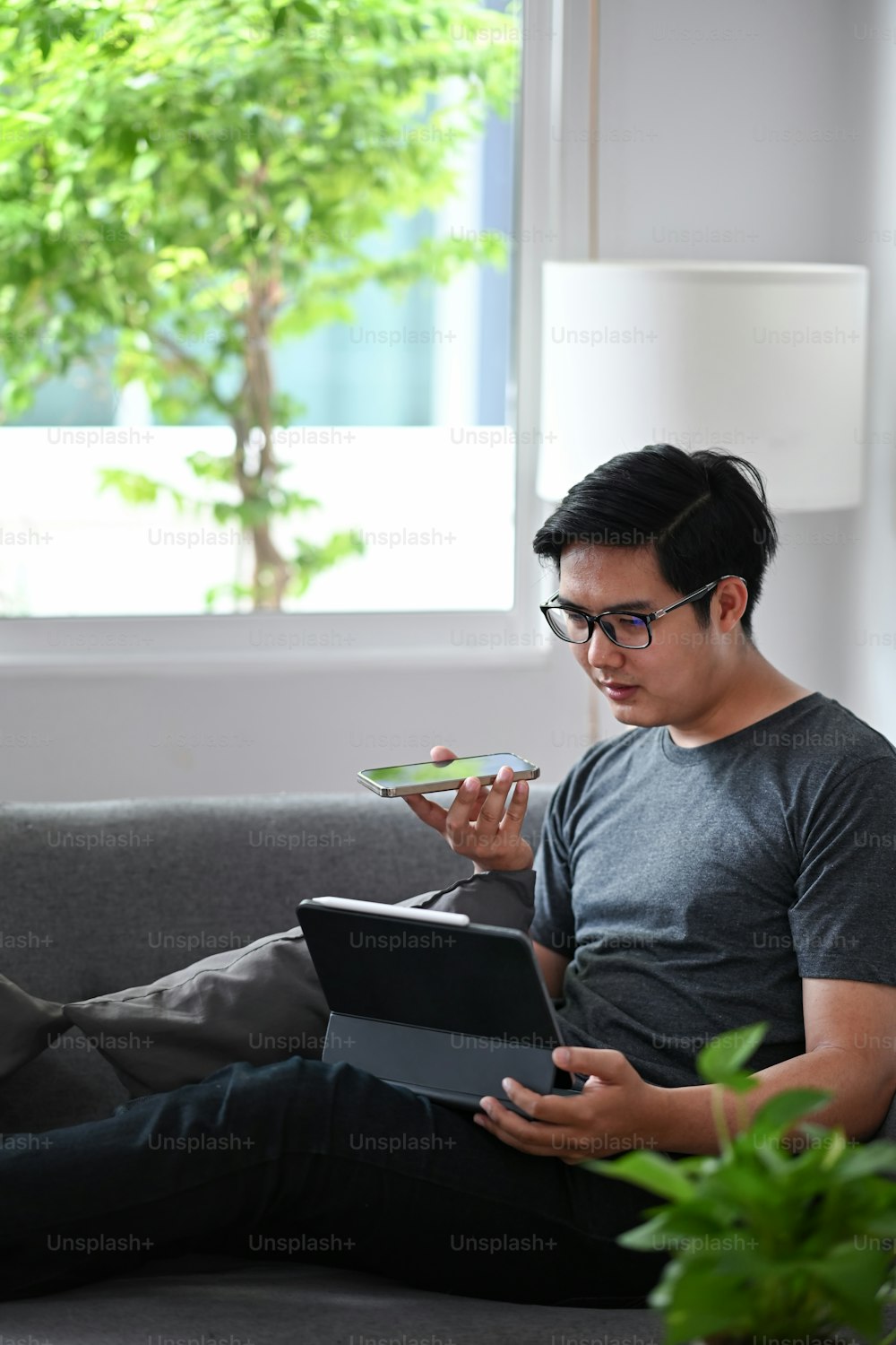 Young man working on computer tablet and talking on mobile phone in living room.