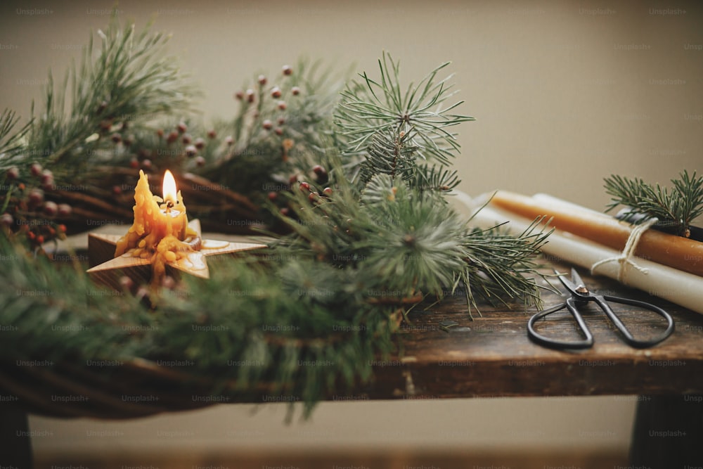 Weihnachtsadvent. Stilvolle brennende Sternkerze im Weihnachtskranz mit Fichtenzweigen und Beeren auf rustikalem Holzhintergrund. Frohe Weihnachten und frohe Feiertage. Atmosphärisches stimmungsvolles Bild