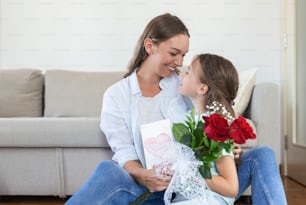 Schönen Muttertag! Die Tochter gratuliert Mama und gibt ihr Postkarte und Blumen. Mama und Mädchen lächeln und umarmen sich. Familienurlaub und Zweisamkeit.
