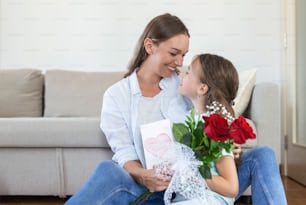 Happy mother's day! Child daughter congratulates mom and gives her postcard and flowers. Mum and girl smiling and hugging. Family holiday and togetherness.