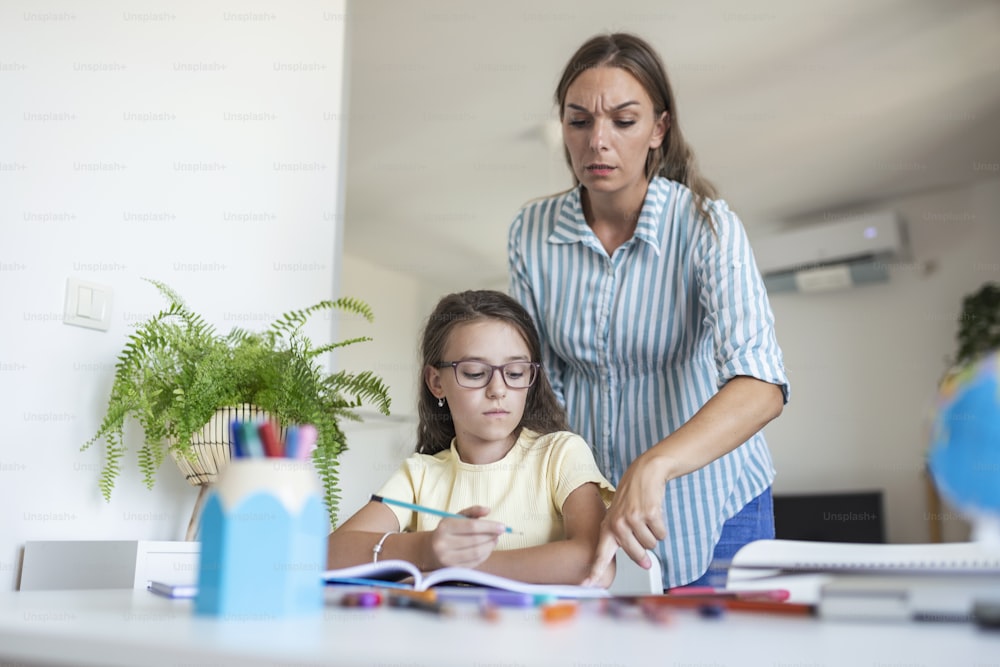 Stressed mother and daughter frustrated over failure homework, school problems concept. Sad little girl turned away from mother, does not want to do boring homework