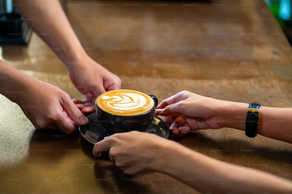 아시아 남자 바리 스타는 카페의 바 카운터에서 고객에게 커피 컵에 뜨거운 커피 라떼를 만들고 있습니다. 남성 커피 숍 웨이터는 고객에게 우유와 함께 뜨거운 커피를 제공합니다. 중소 기업 식당 주인 개념입니다.