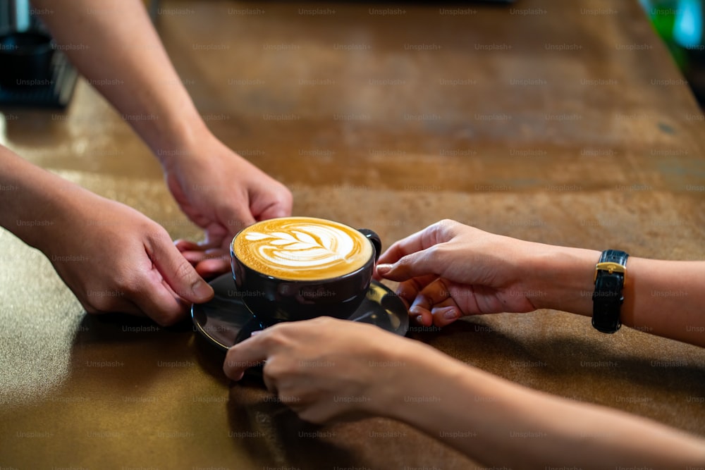 Asian man barista making hot coffee latte in coffee cup to customer on bar counter at cafe. Male coffee shop waiter serving hot coffee with milk to client. Small business restaurant owner concept.