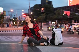 밤에 도시 거리에 앉아 있는 쾌활한 아시아 여성.
