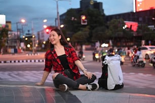 Cheerful Asian woman sitting on city street at night.