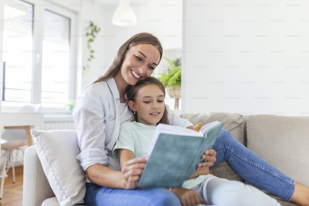 Loving young mother reading book to adorable little daughter, sitting on cozy sofa in living room, mum teaching preschool girl child, family spending weekend at home together, children education