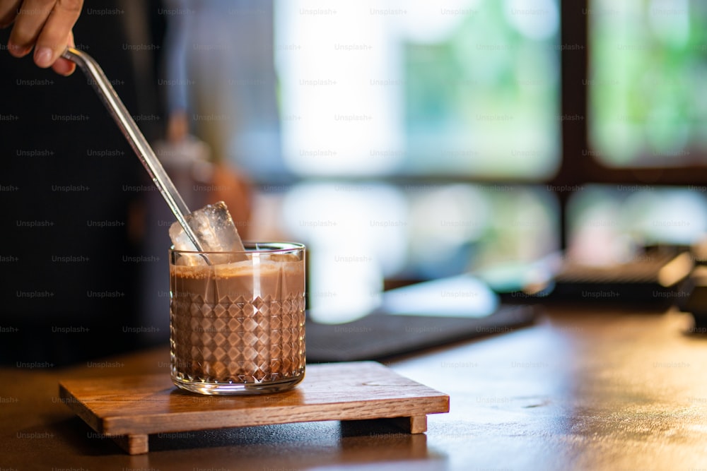 Asian woman barista make iced cocoa with froth milk in the glass on counter. Female coffee shop waitress employee preparing cold drink for customer at cafe. Small business coffee shop owner concept.