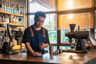 Asian man barista using towel sweeping counter bar with alcohol sanitizer before opening cafe. Male waiter cleaning up coffee shop for service to customer. Small business owner working concept