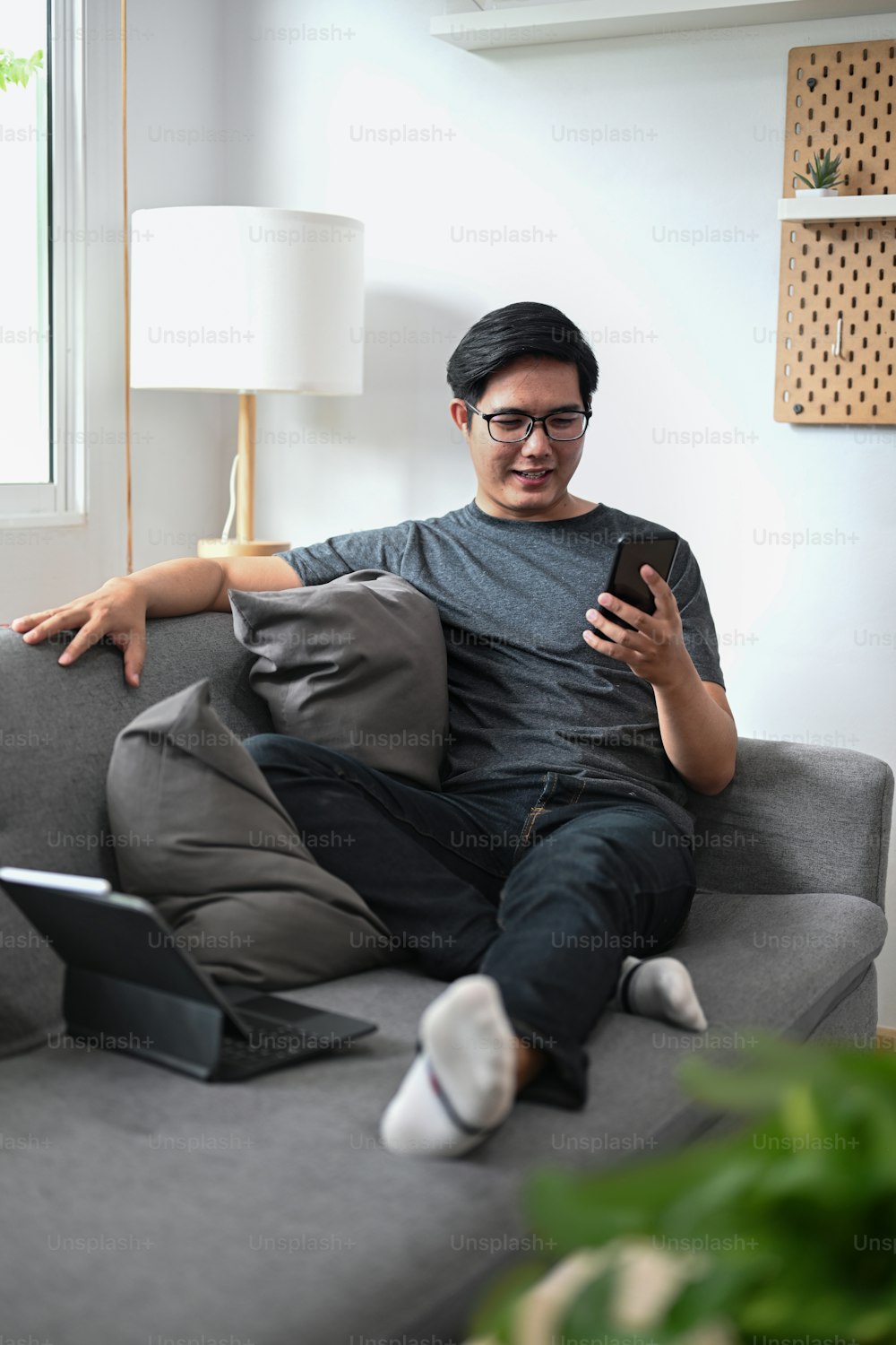 Young Asian man sitting on sofa and using smart phone.