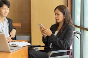 Mujer de negocios en silla de ruedas relajándose en un teléfono móvil inteligente después de terminar la reunión en la sala de reuniones
