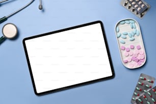 Mock up digital tablet with white screen, stethoscope and medical pills on blue background.