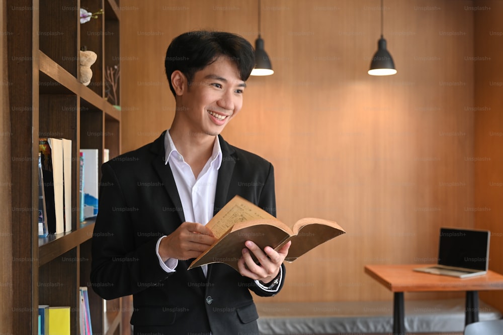 本を持ち、現代の職場に立っている笑顔のビジネスマン。