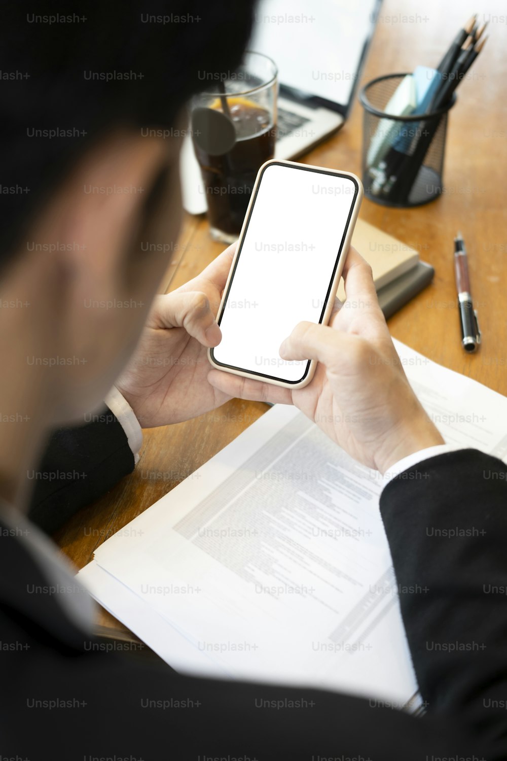 Over the shoulder view of businessman sitting at office desk and using smart phone.