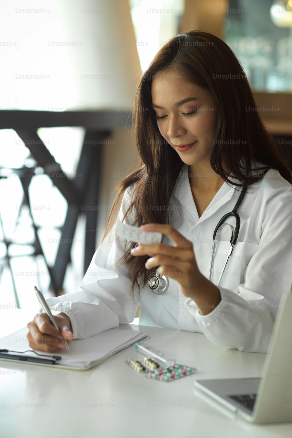 Femme médecin ou pharmacienne rédigeant une ordonnance sur papier, tenant des pilules ou des médicaments dans une clinique