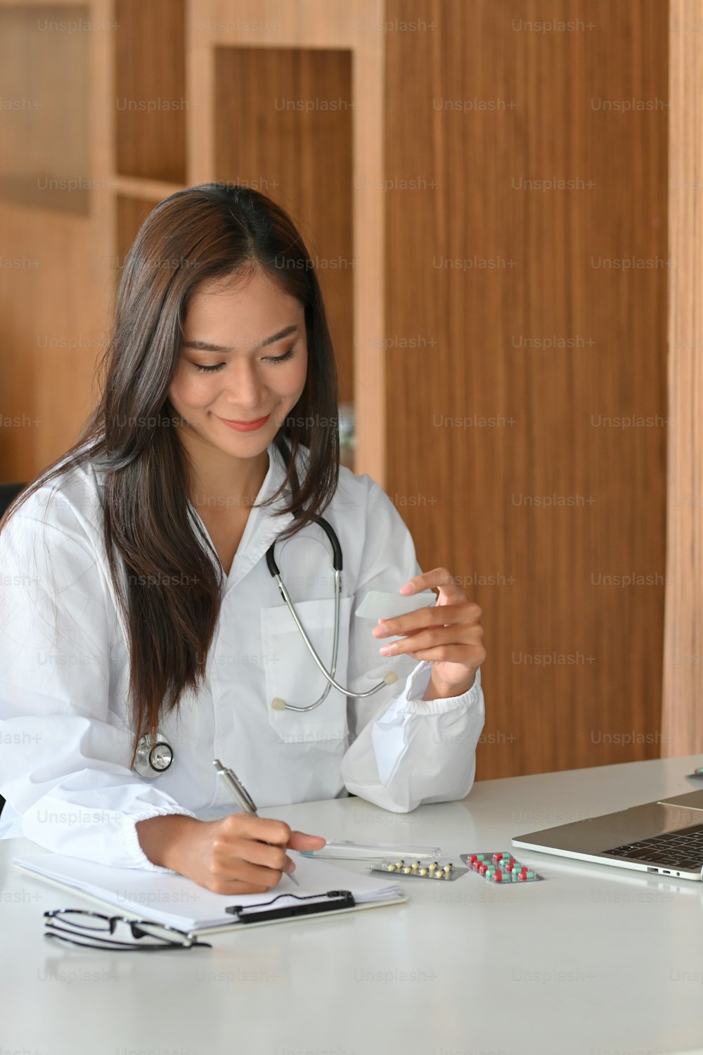 Young asian female pharmacist holding a pack of pills, tablet blisters, medicine and writing a drugs prescription on paper
