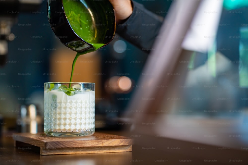 Asian woman barista making matcha green tea with fresh milk in the glass. Female coffee shop waitress serving iced matcha latte to customer on counter at cafe. Small business coffee shop owner concept