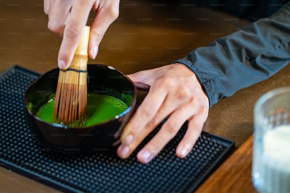 Barista donna asiatica che prepara il tè verde matcha con latte fresco nel bicchiere. Cameriera di caffetteria femminile che serve latte matcha ghiacciato al cliente sul bancone del bar. Concetto di proprietario di una caffetteria per piccole imprese