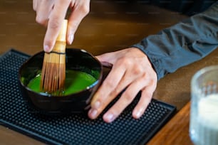 Asian woman barista making matcha green tea with fresh milk in the glass. Female coffee shop waitress serving iced matcha latte to customer on counter at cafe. Small business coffee shop owner concept