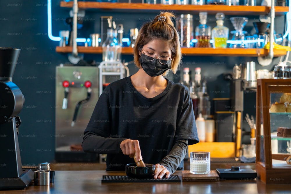 아시아 여성 바리스타가 잔에 신선한 우유로 말차 녹차를 만들고 있다. 여성 커피 숍 웨이트리스는 카페의 카운터에서 고객에게 아이스 말차 라떼를 제공합니다. 중소 기업 커피 숍 소유자 개념