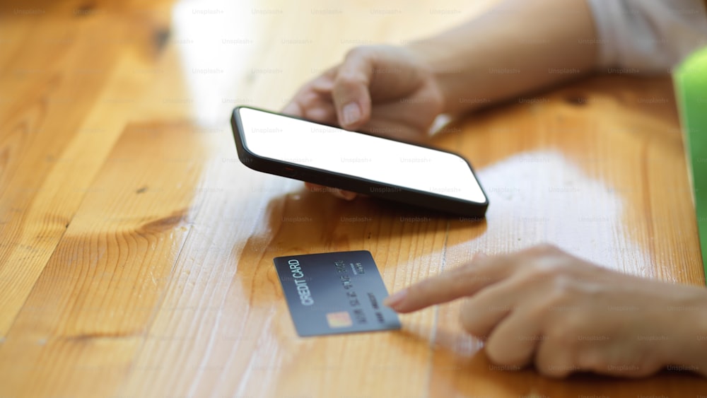 テーブルの上にスマートフォンとクレジットカードを持つ女性の手の接写側面図。デジタルウォレット, 非接触型, オンライン決済