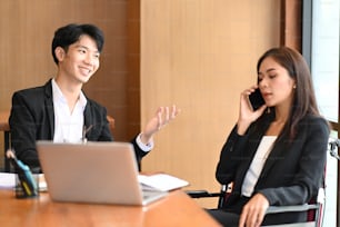 Disabled businesswoman in wheelchair talking on mobile phone while sitting with colleagues in modern office.