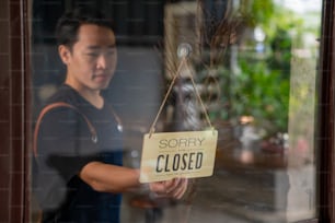 Homme asiatique barista de café marchant vers la porte du café et tournant le signe fermé suspendu pour ouvrir. Serveur masculin préparant le service de restaurant à la clientèle. Propriétaire d’une petite entreprise et concept de travail à temps partiel