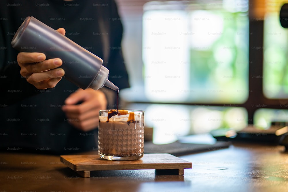 Une barista asiatique fait du cacao glacé avec de la mousse de lait dans le verre sur le comptoir. Serveuse d’un café préparant une boisson fraîche pour un client au café. Concept de propriétaire de café de petite entreprise.
