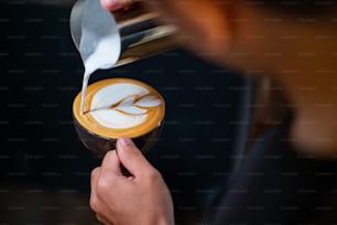 Close up hand of man barista pouring froth milk in espresso coffee in coffee cup making coffee latte art serve to customer. Small business cafe and restaurant owner and part time job working concept