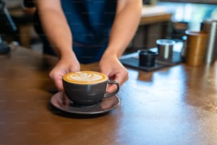 Asian man barista making hot coffee latte in coffee cup to customer on bar counter at cafe. Male coffee shop waiter serving hot coffee with milk to client. Small business restaurant owner concept.