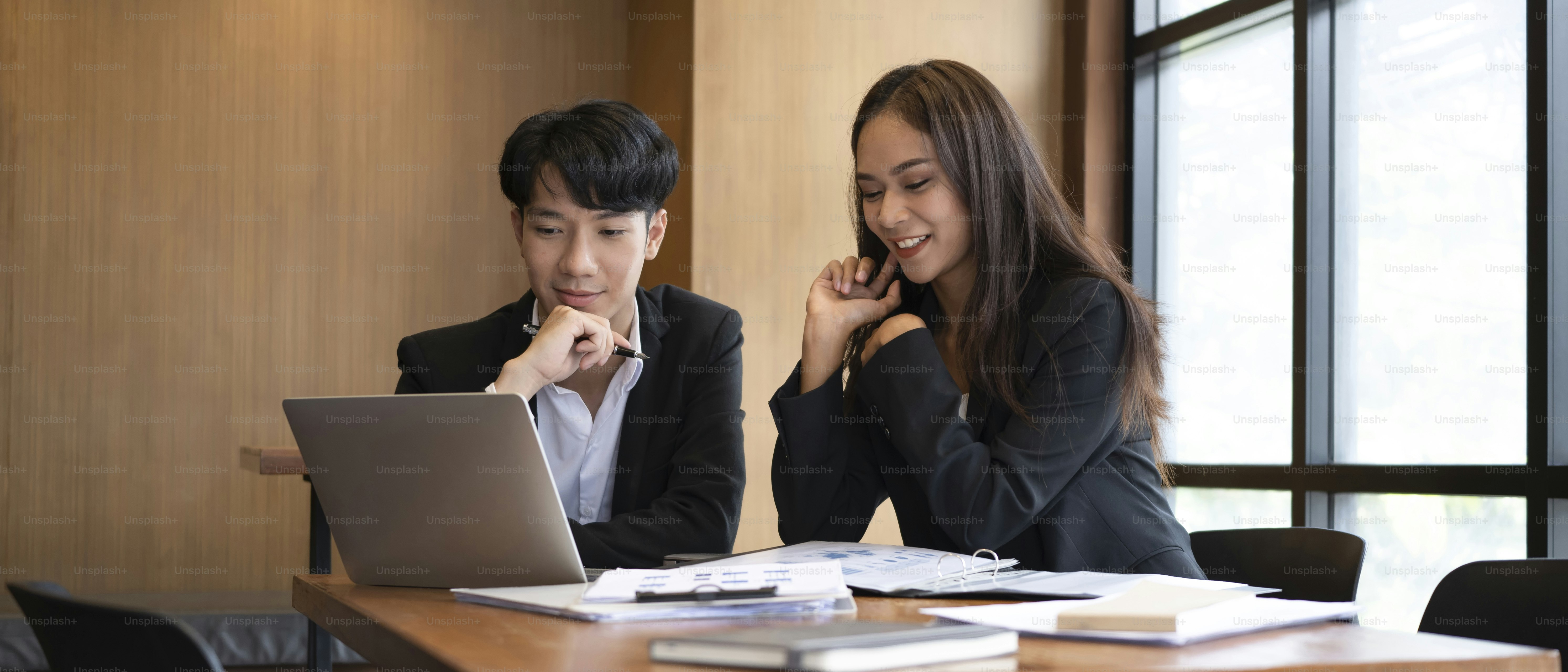 Two young business people  discussing financial data on computer laptop together in office.