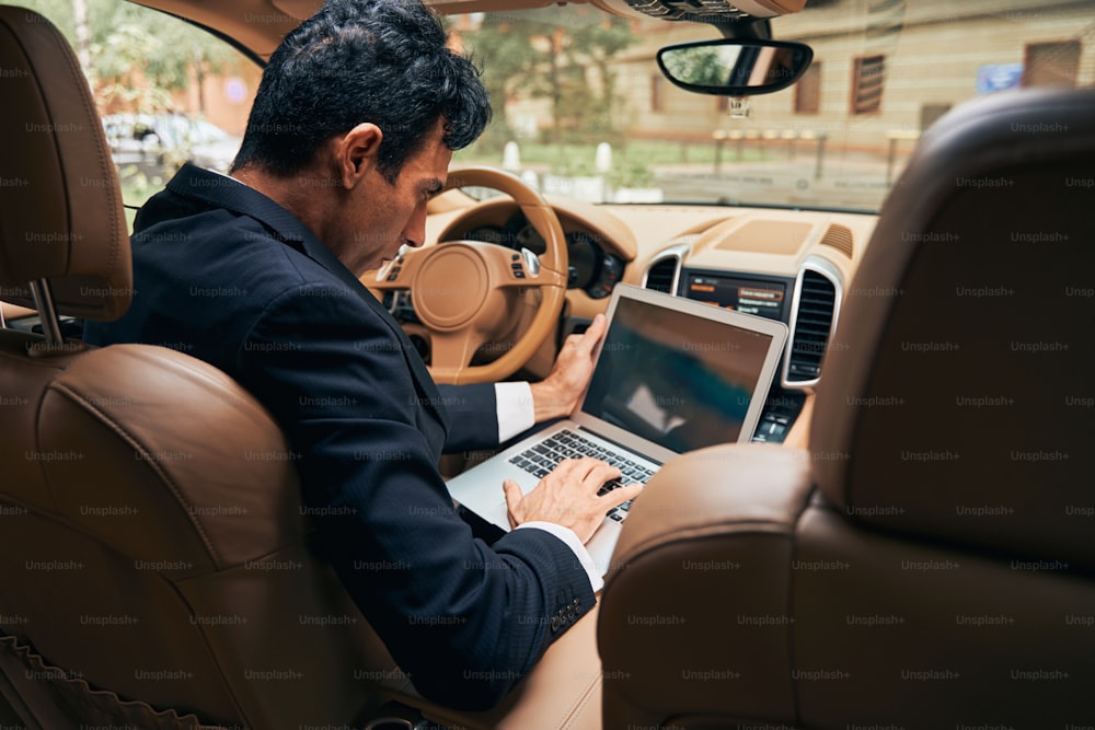 Vista dal sedile posteriore dell'auto dell'uomo usando il computer portatile e facendo clic sulla tastiera