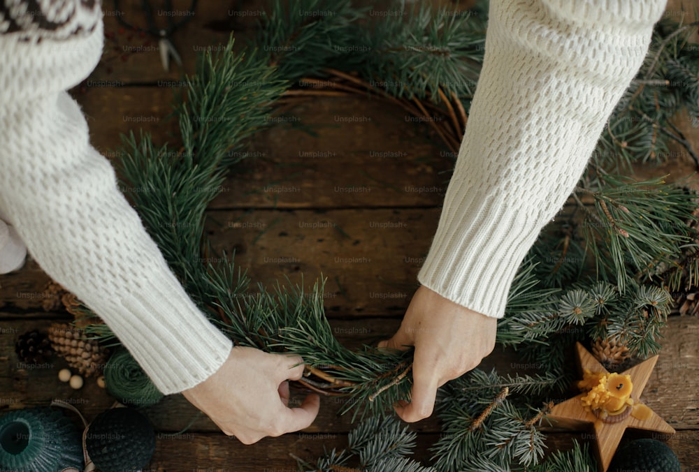 Mains de femme tenant des branches de pin et arrangeant une couronne de Noël sur fond en bois rustique avec des pommes de pin, des ciseaux, une bougie. Vue de dessus. Préparatifs des vacances d’hiver. Atelier festif