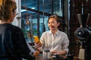 Modern Asian woman using smartphone scanning bar code making contactless payment checkout her coffee at coffee shop. Small business owner with electronic mobile banking contactless payment concept