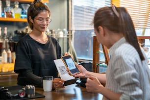 スマートフォンのスキャンバーコードを使用して、非接触型決済を行う現代のアジア人女性がコーヒーショップでコーヒーをチェックアウトします。電子モバイルバンキングの非接触型決済コンセプトを持つ中小企業の経営者