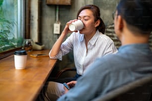 Asian businessman and businesswoman meeting with discussion business plan at coffee shop. Smiling man and woman friends drinking coffee with talking together. Small business and restaurant concept.