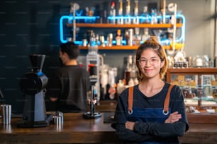 Porträt des Vertrauens Asiatische Coffeeshop-Barista, die mit verschränkten Armen vor der Bartheke steht und glücklich in die Kamera schaut. Kleinunternehmer und Cafébesitzer-Konzept