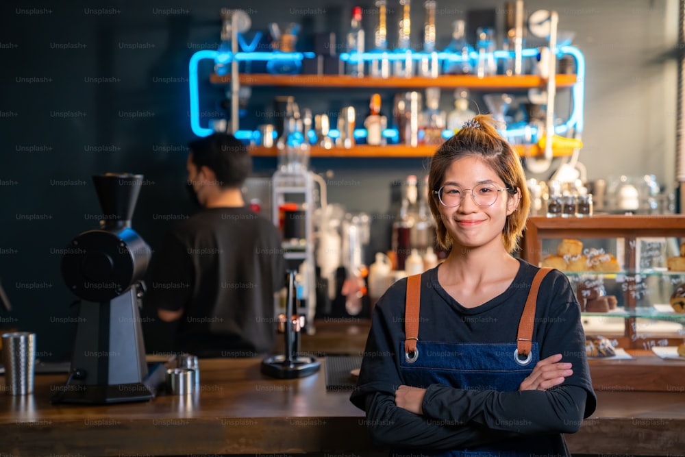 자신감의 초상화 아시아 여성 커피숍 바리스타가 바 카운터 앞에 서서 팔짱을 끼고 행복으로 카메라를 바라보고 있다. 중소 기업 식당 기업가 및 카페 소유자 개념