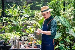 温室の庭で観葉植物と花を世話するアジアの男性の庭師。店頭で植物の注文を数えたりチェックしたりする男性植物店主。中小企業の起業家と環境植物の思いやりのコンセプト。